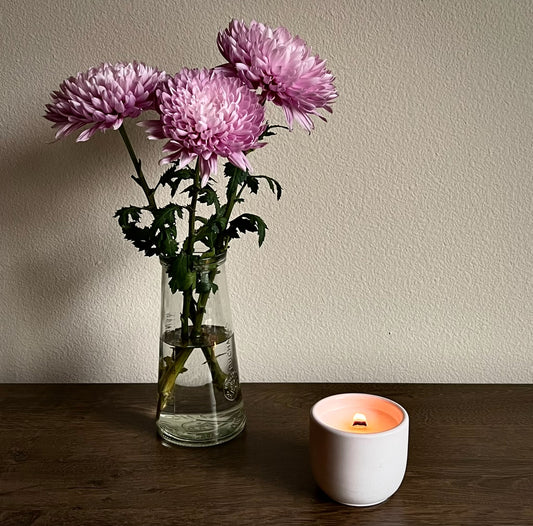 burning candle in a cement jar with flower bouquet in the background 